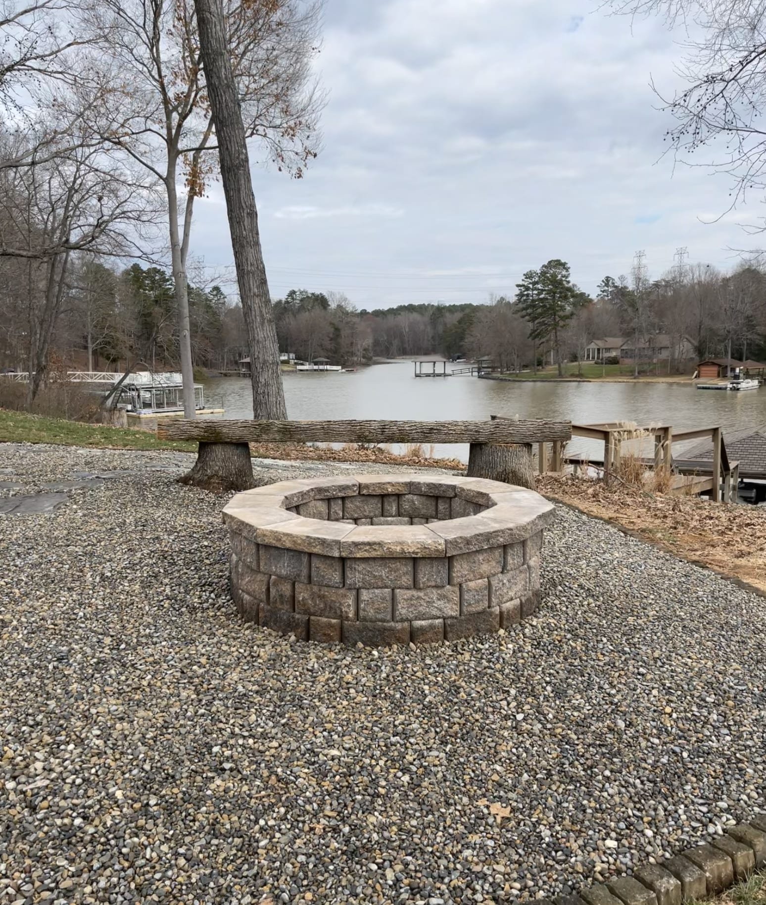 Custom stacked-stone fire pit on a gravel patio overlooking a lake.