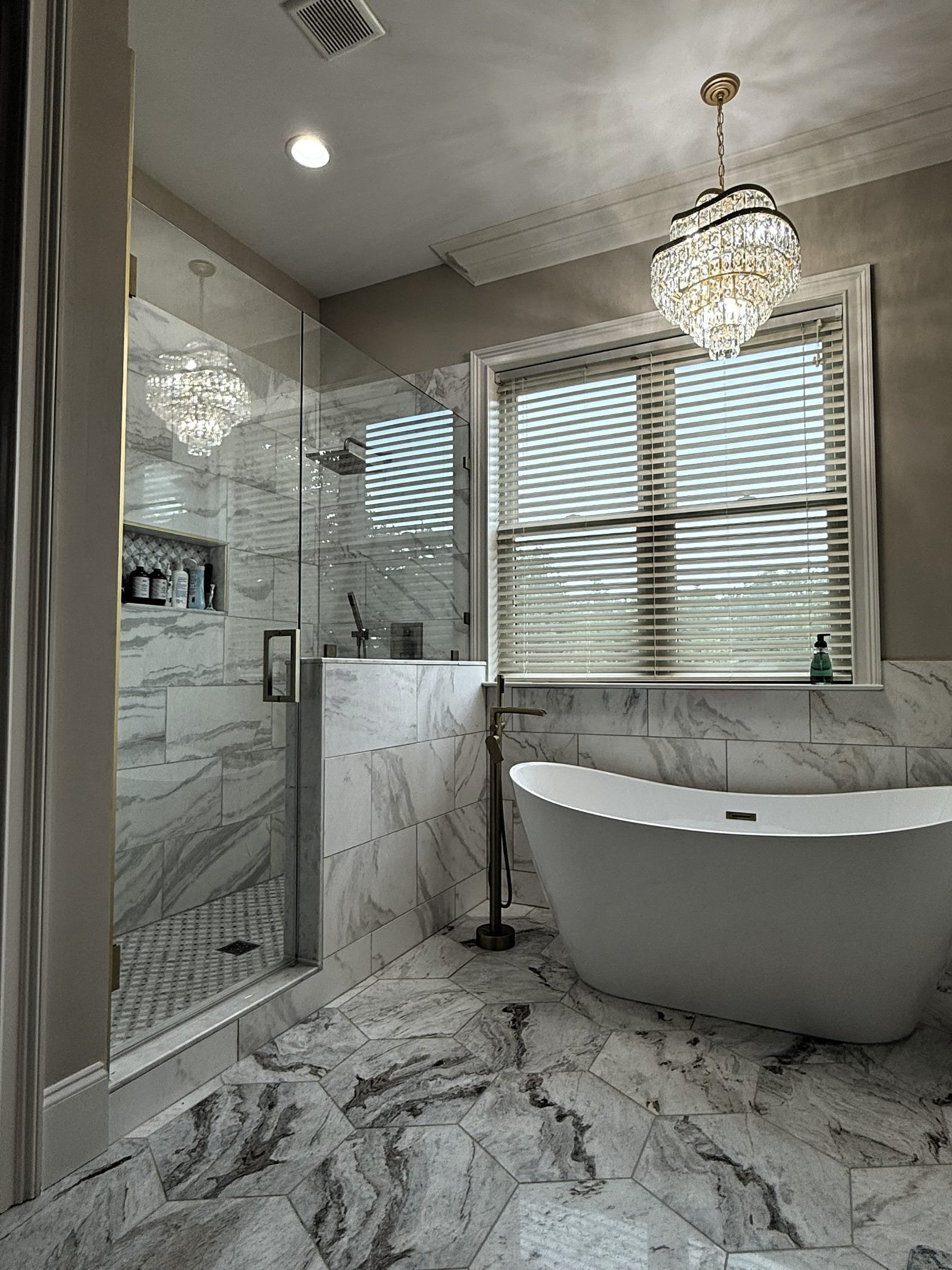 Remodeled bathroom with a freestanding soaking tub, marble tile, and crystal chandelier.